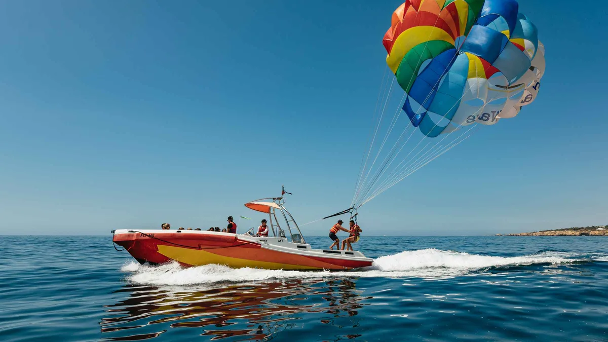 Parasailer lifted high above the blue bay off Albufeira with the beach and cliffs below, one of the more adrenaline-driven things to do in Albufeira, Algarve